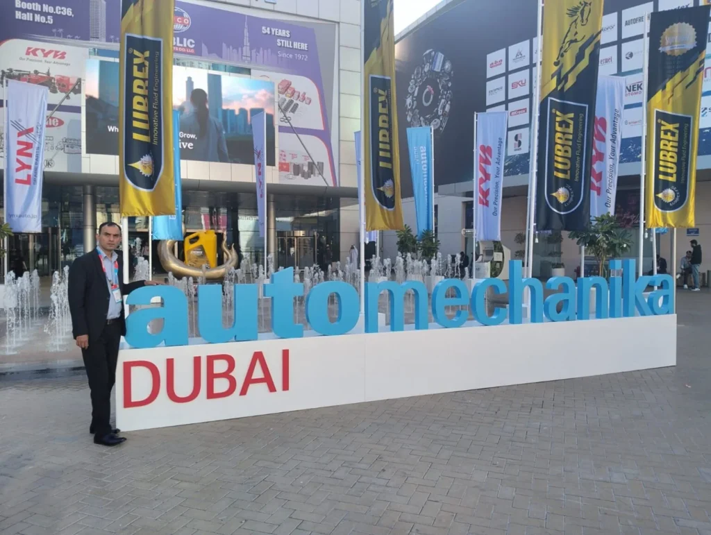 Representative of Maxtron Tyres attending Automechanika Dubai, standing beside the event signage at Dubai World Trade Centre.
