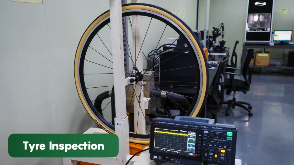 Bicycle wheel mounted on tyre inspection equipment in a quality testing laboratory, evaluating tyre performance, balance, and manufacturing accuracy.