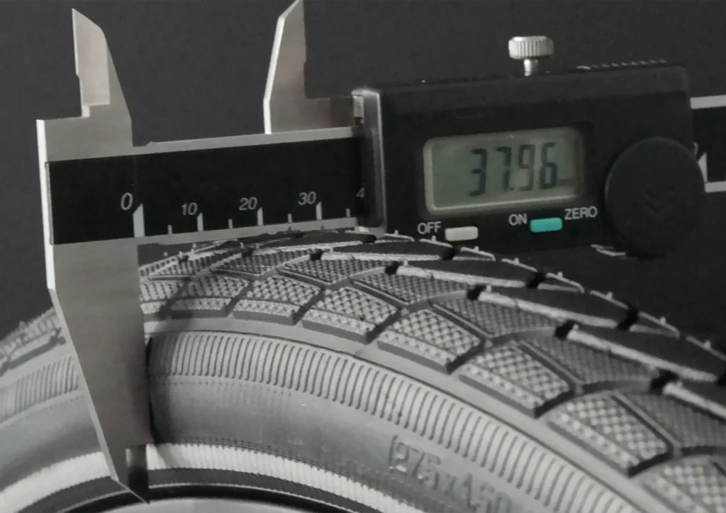Digital caliper measuring the dimensions of a bicycle tyre during quality inspection, demonstrating precision quality control and manufacturing accuracy.